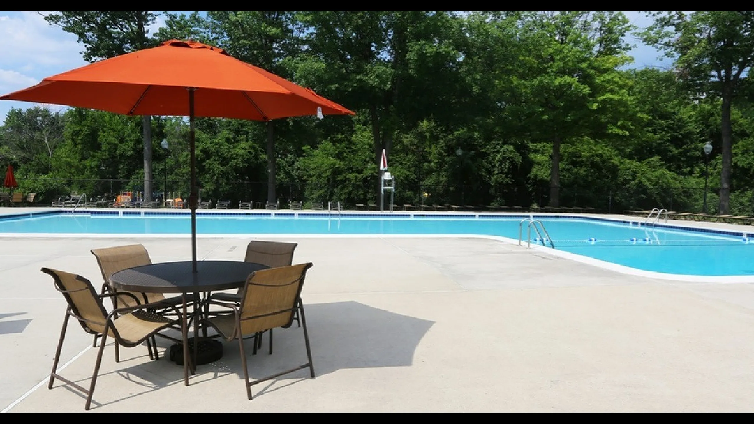 Inviting outdoor pool area with vibrant orange umbrella and elegant seating, surrounded by lush greenery for a serene retreat.