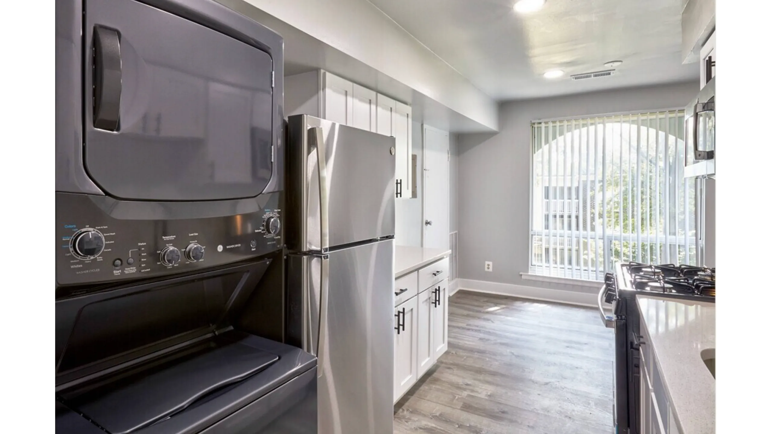 Modern kitchen with sleek stainless steel appliances, in-unit washer and dryer, bright natural light, and elegant grey flooring.