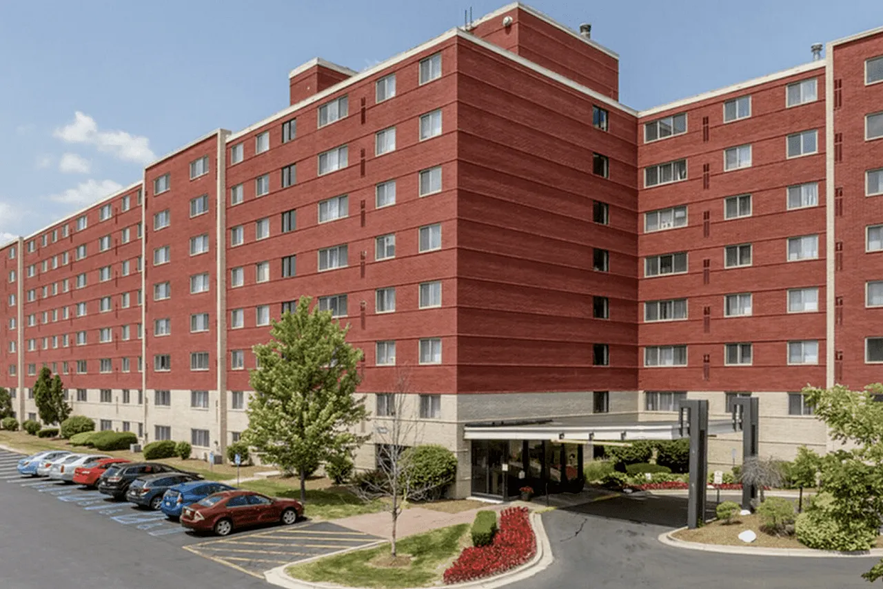 Charming red-brick apartment complex with sleek lines and lush landscaping, boasting ample parking and a welcoming entrance.