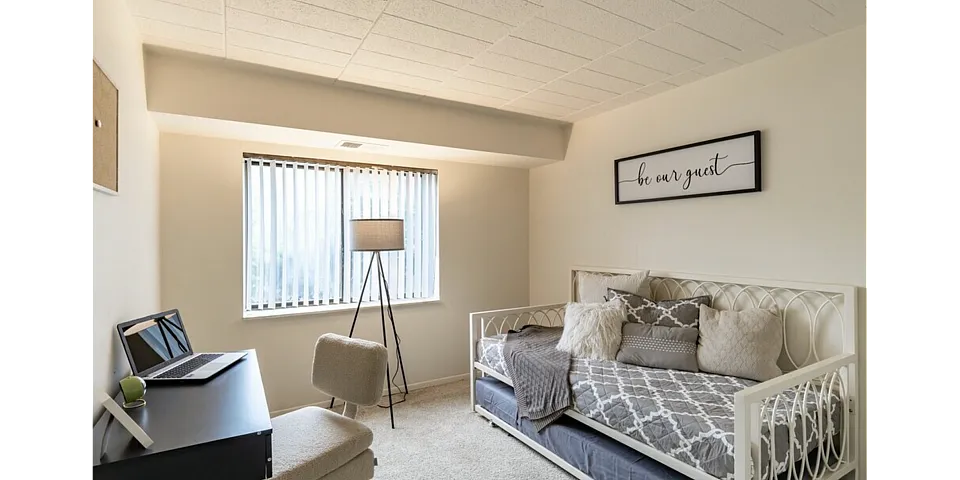 Cozy guest room with stylish daybed, modern workspace, and a flood of natural light, perfect for relaxation and productivity.