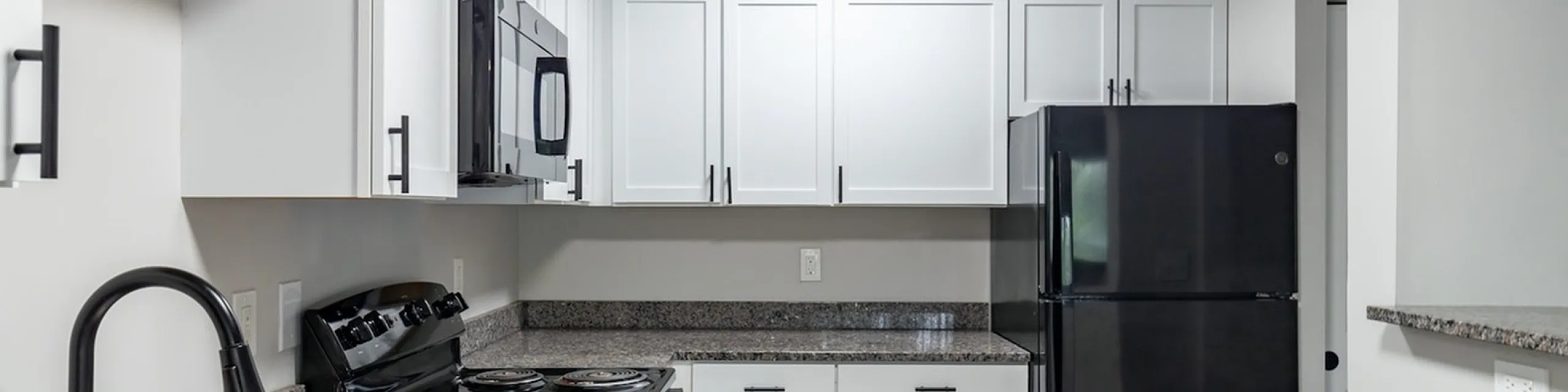 Modern kitchen with sleek black appliances, stylish white cabinetry, and elegant granite countertops.