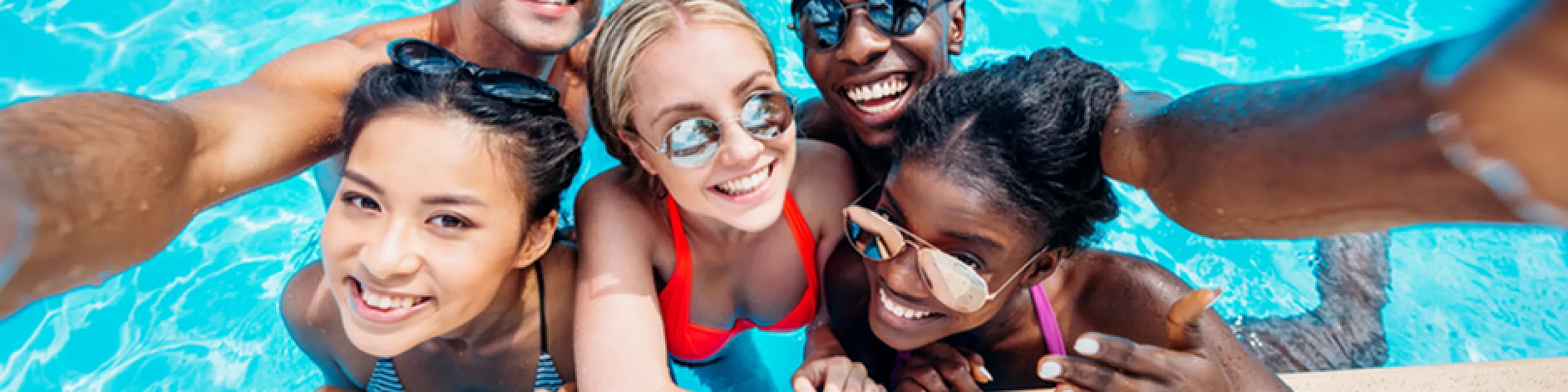 Joyful group of friends taking a selfie at a vibrant swimming pool, highlighting social fun and summer relaxation.