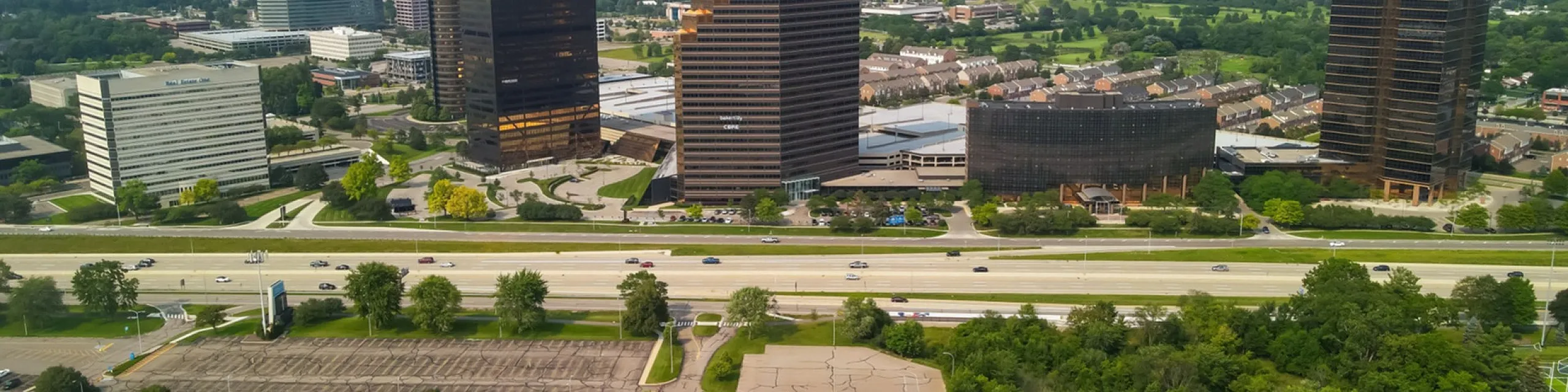 Aerial view of modern office buildings surrounded by lush greenery and a bustling highway, showcasing a vibrant urban landscape.