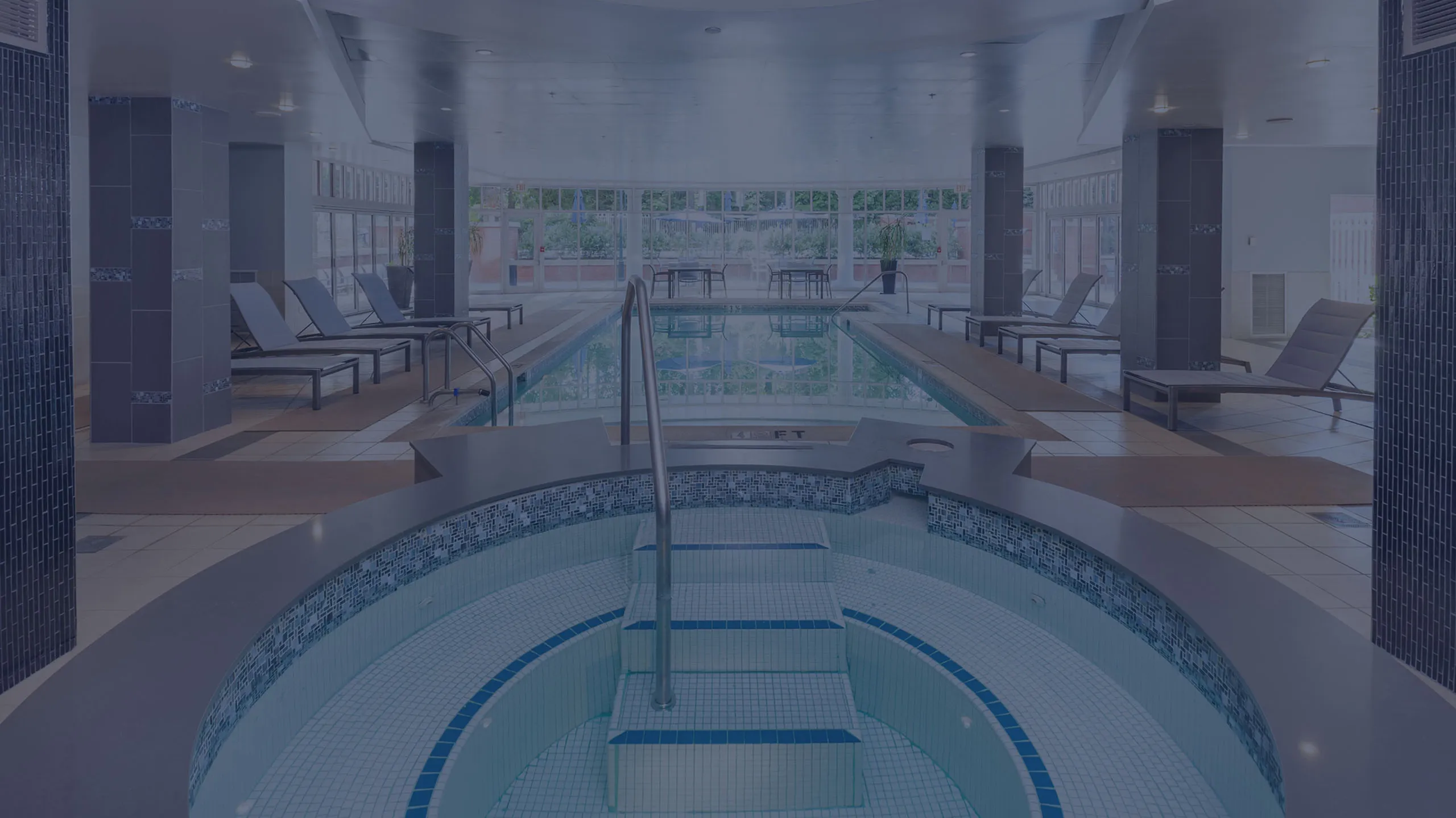 Luxurious indoor pool area featuring a spacious swimming pool, elegant columns, and comfortable lounge chairs, perfect for relaxation.