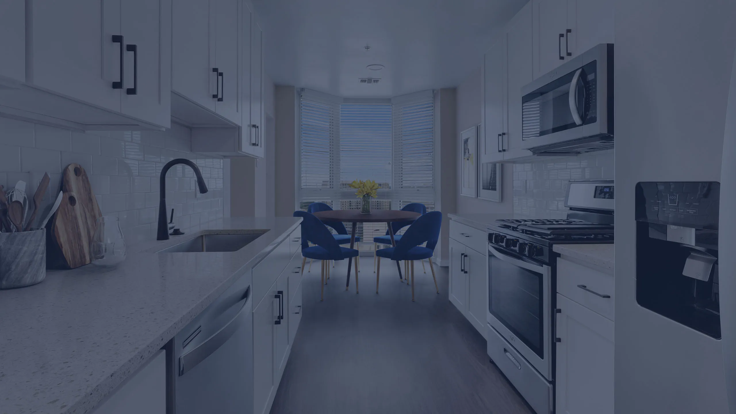 Modern kitchen with sleek white cabinets, elegant countertops, stainless steel appliances, and a cozy dining nook with vibrant blue chairs and a picturesque window view.