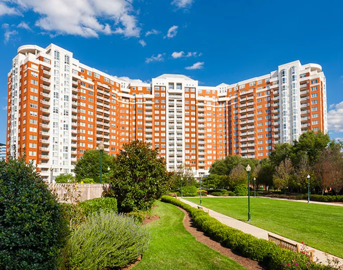 Elegant high-rise apartment building with modern architecture surrounded by lush green gardens and a clear blue sky.
