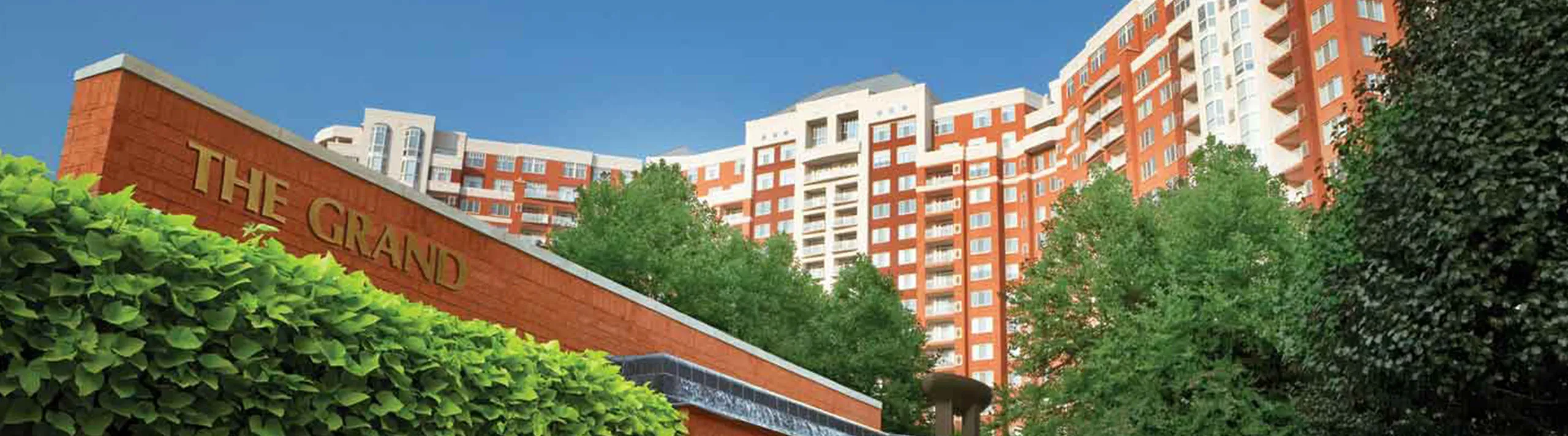 Elegant apartment complex 'The Grand' featuring modern architecture surrounded by lush greenery.