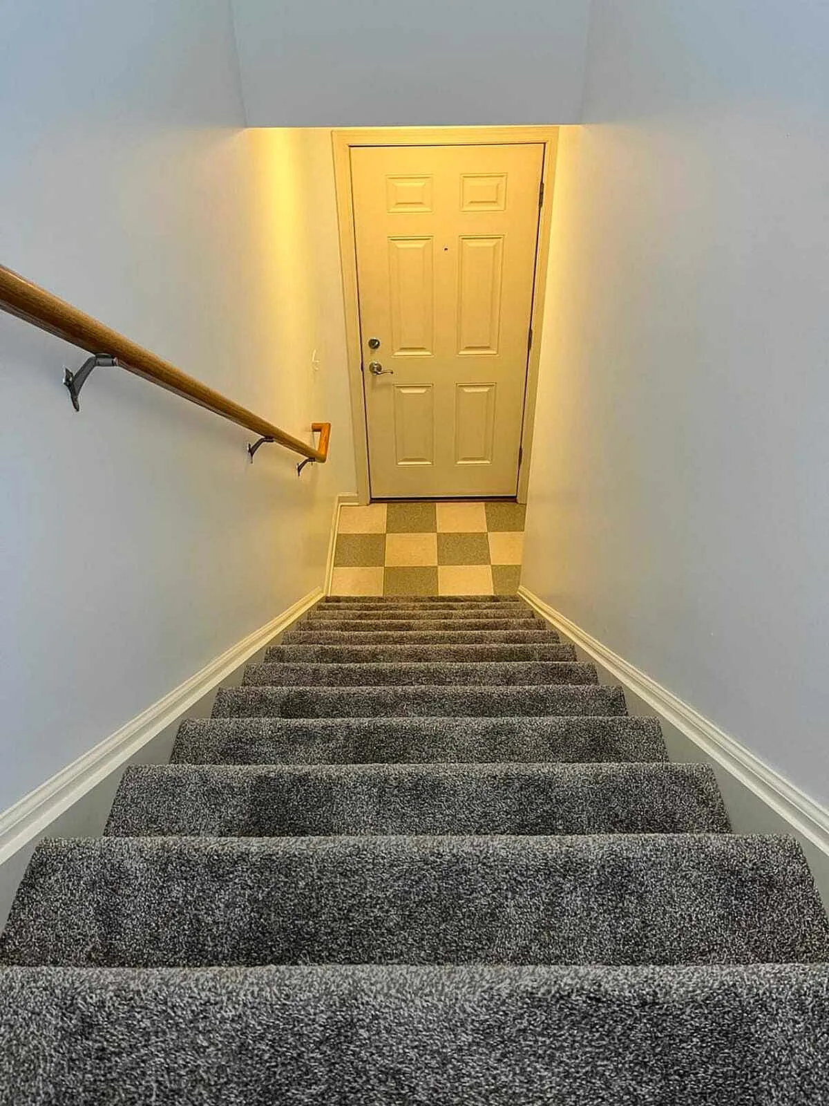 Inviting staircase with plush carpet leading to a warmly lit entrance door, offering a cozy welcome home.