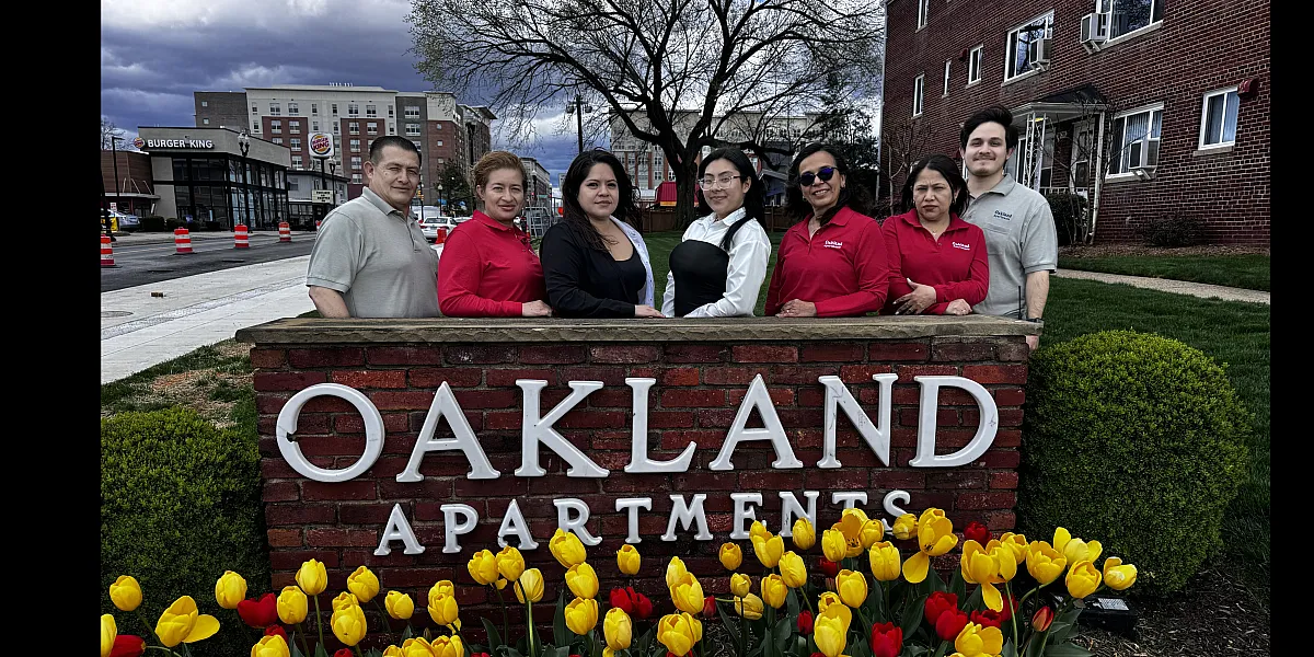 Welcoming Oakland Apartments staff standing proudly by a vibrant sign with colorful tulips, capturing a friendly and inviting atmosphere.