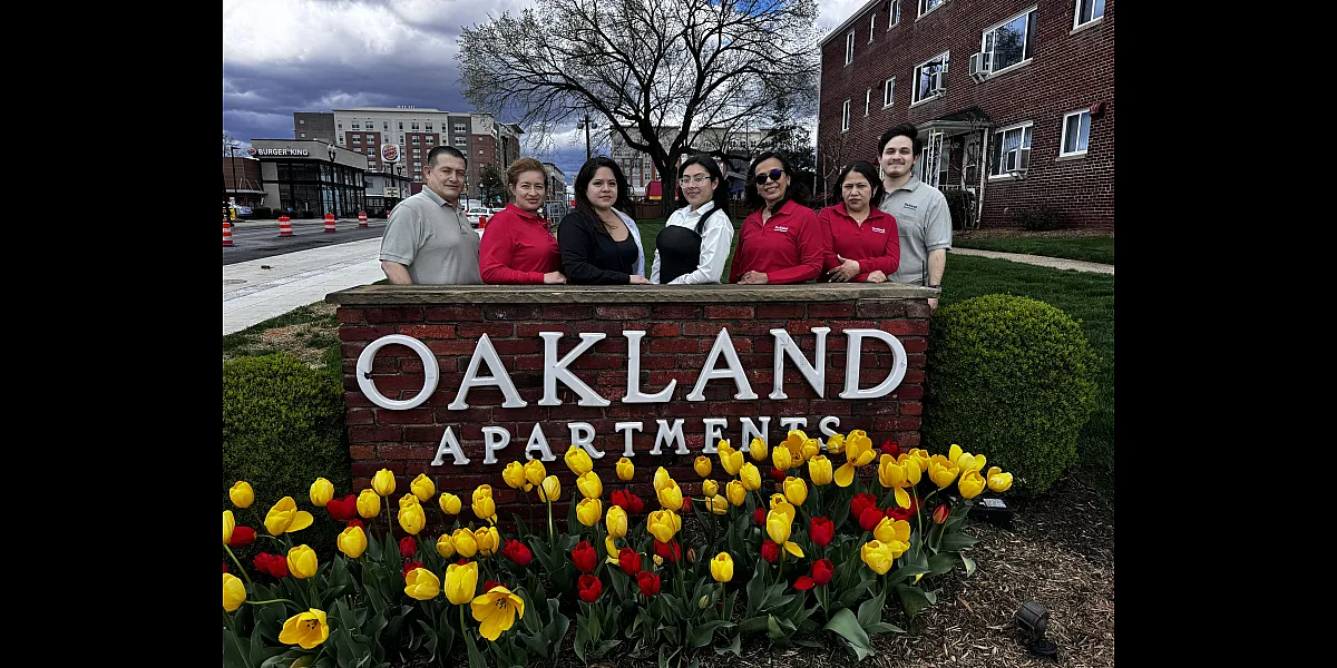 Welcoming Oakland Apartments team posing cheerfully in front of a vibrant garden with red and yellow tulips.