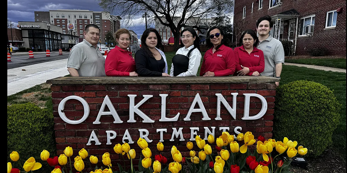 Welcoming team standing by the Oakland Apartments sign, framed by vibrant yellow and red tulips, showcasing community and charm.
