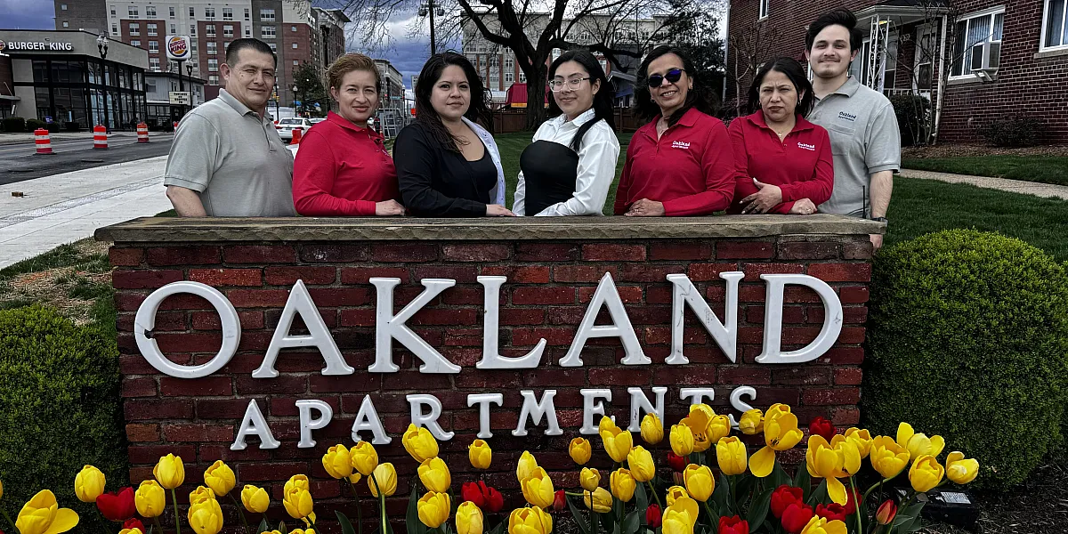Welcoming Oakland Apartments team standing behind a charming brick sign, surrounded by vibrant yellow and red tulips, with a residential building in the background.