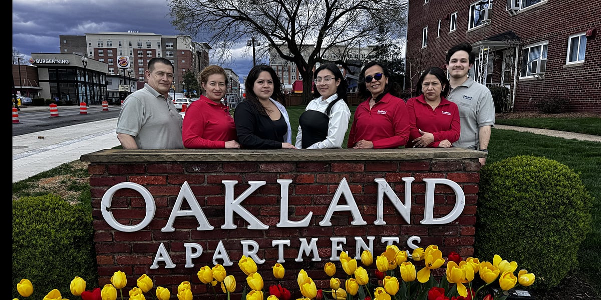 Friendly Oakland Apartments team standing proudly behind the vibrant tulip garden and welcoming signage, showcasing a community-focused atmosphere.
