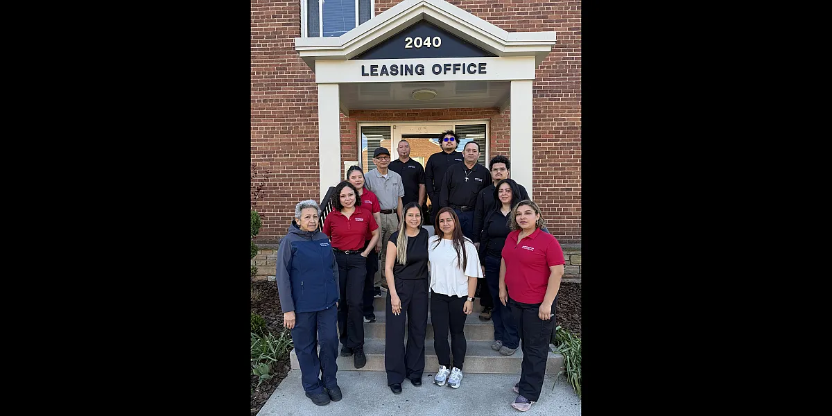 Welcoming leasing office team standing in front of a brick building labeled '2040 LEASING OFFICE', ready to assist potential tenants.