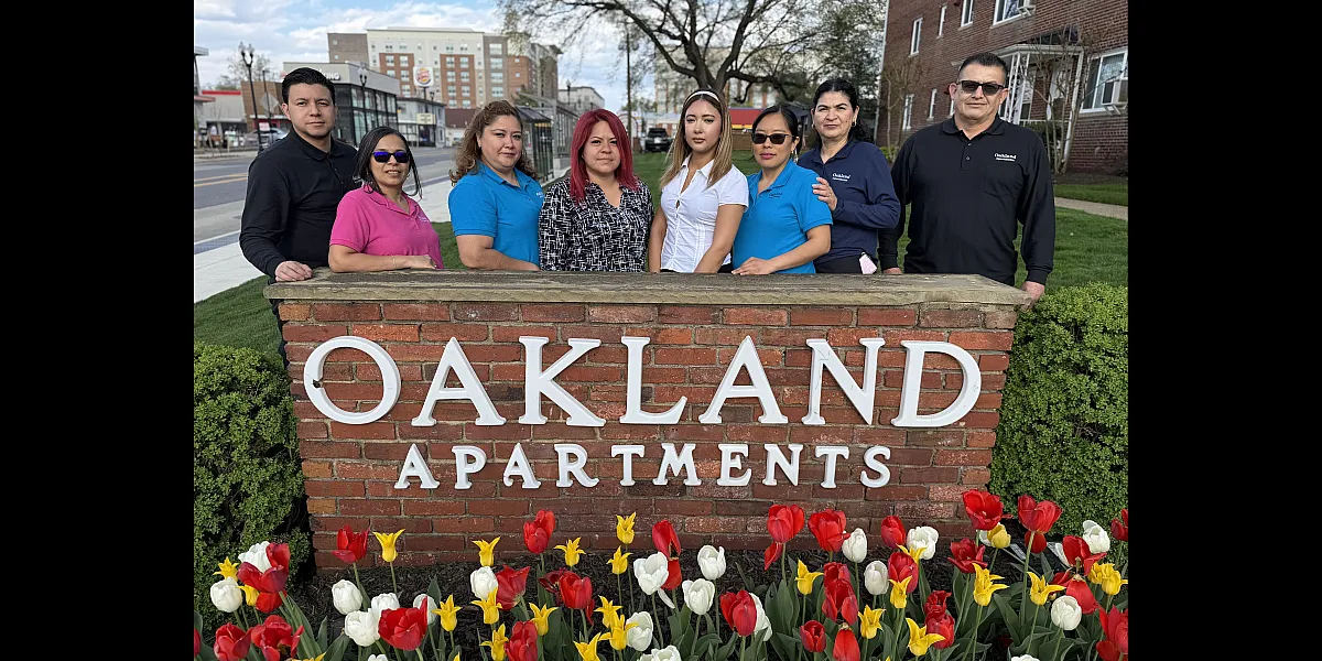Team standing proudly in front of the Oakland Apartments sign, surrounded by vibrant tulips, showcasing a welcoming community.