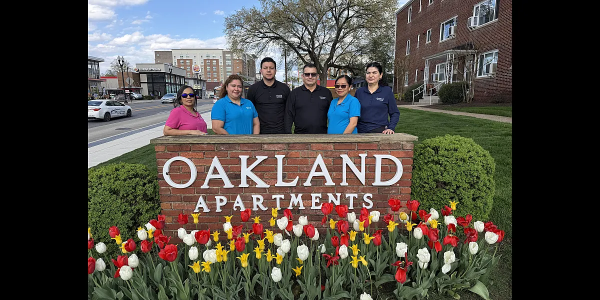 Charming Oakland Apartments sign surrounded by vibrant tulips, with a friendly team standing proudly in front, embodying the community spirit.