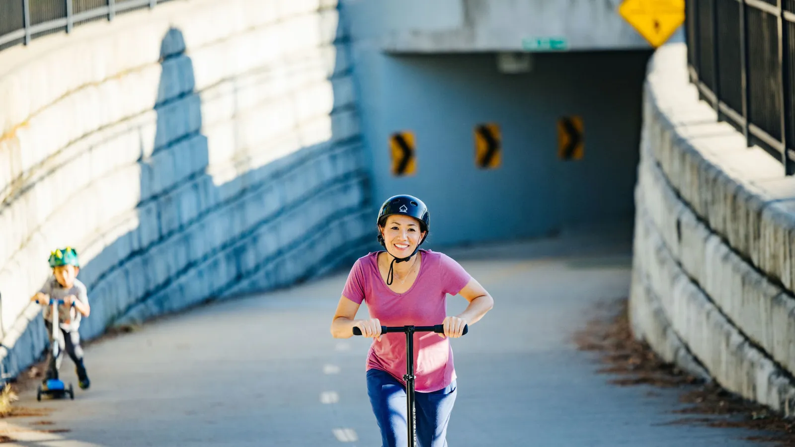 A smiling woman helps a laughing boy put on a bike helmet