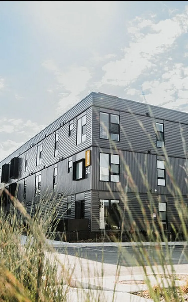 Contemporary apartment building with sleek black exterior and large windows, set against a bright sky.