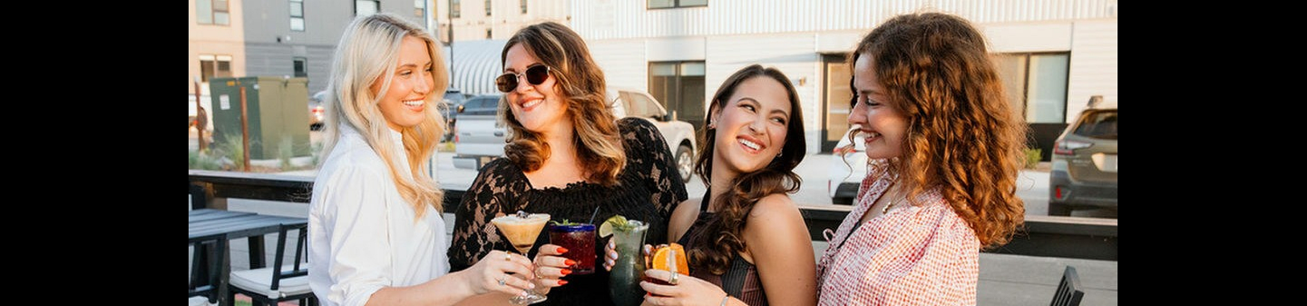 Vibrant social gathering with four people enjoying cocktails outdoors, set against the backdrop of modern apartment buildings, highlighting a lively community atmosphere.