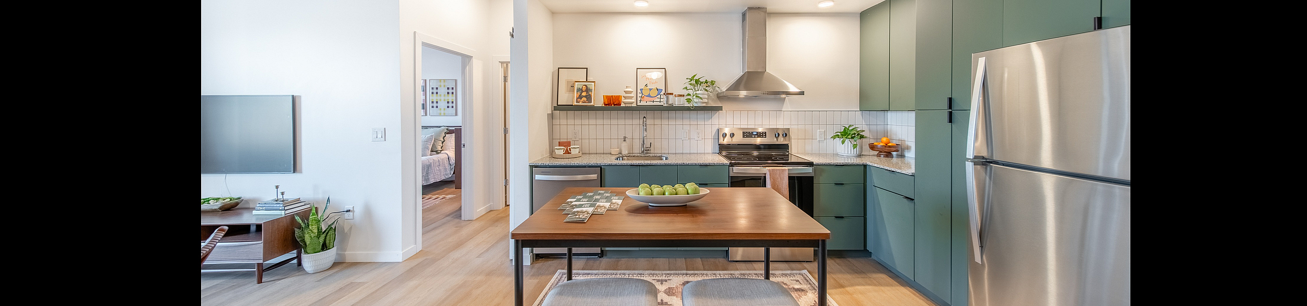 Contemporary open-concept kitchen with stylish green cabinets, stainless steel appliances, and chic dining area featuring a wooden table and cushioned stools.