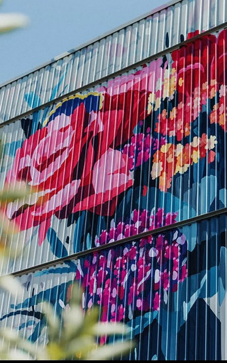 Vibrant apartment exterior adorned with a stunning floral mural featuring bold red, pink, and purple flowers, adding artistic charm to urban living.