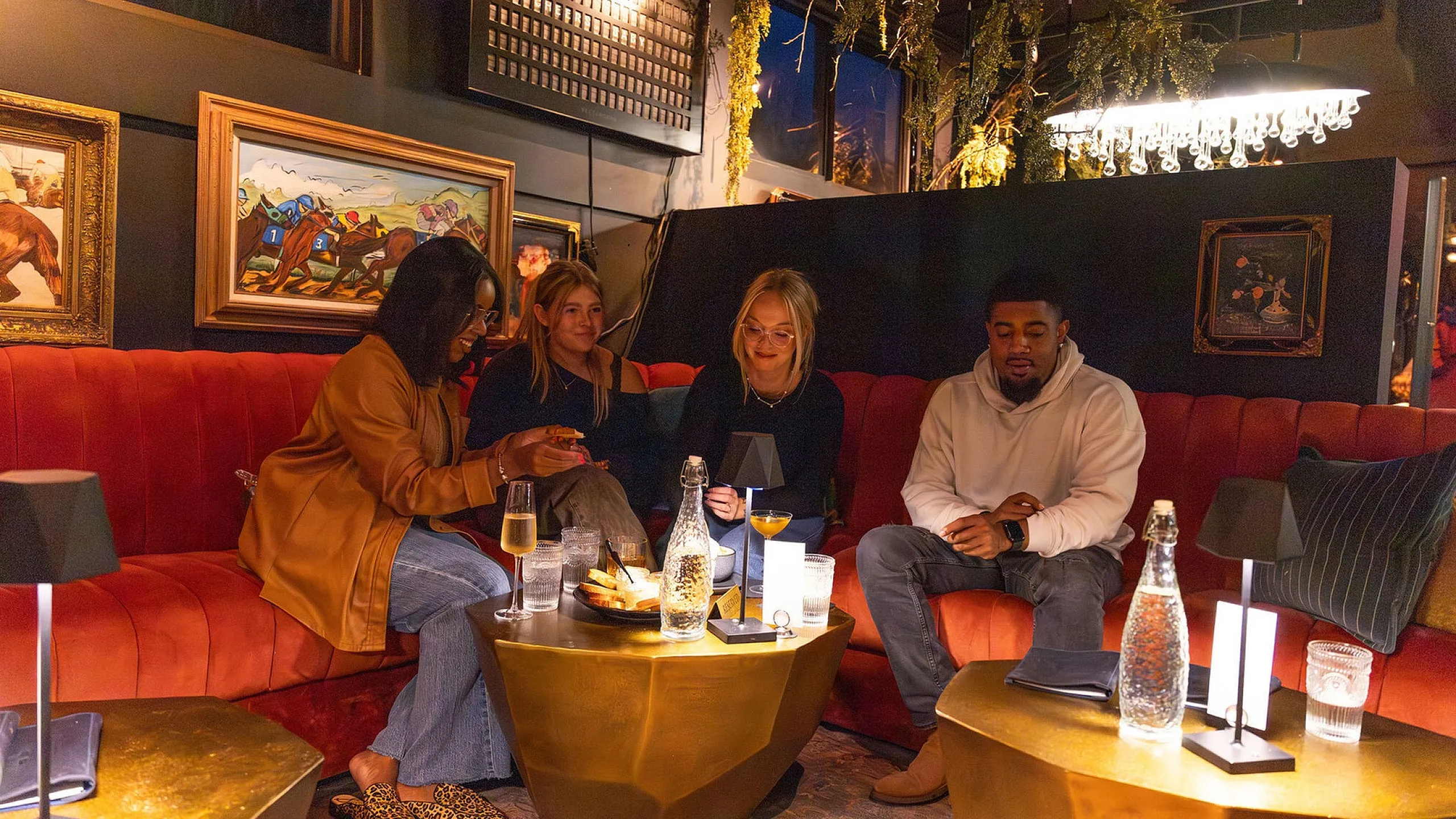 Stylish lounge atmosphere with friends enjoying drinks on a cozy red sofa surrounded by elegant artworks and soft lighting.