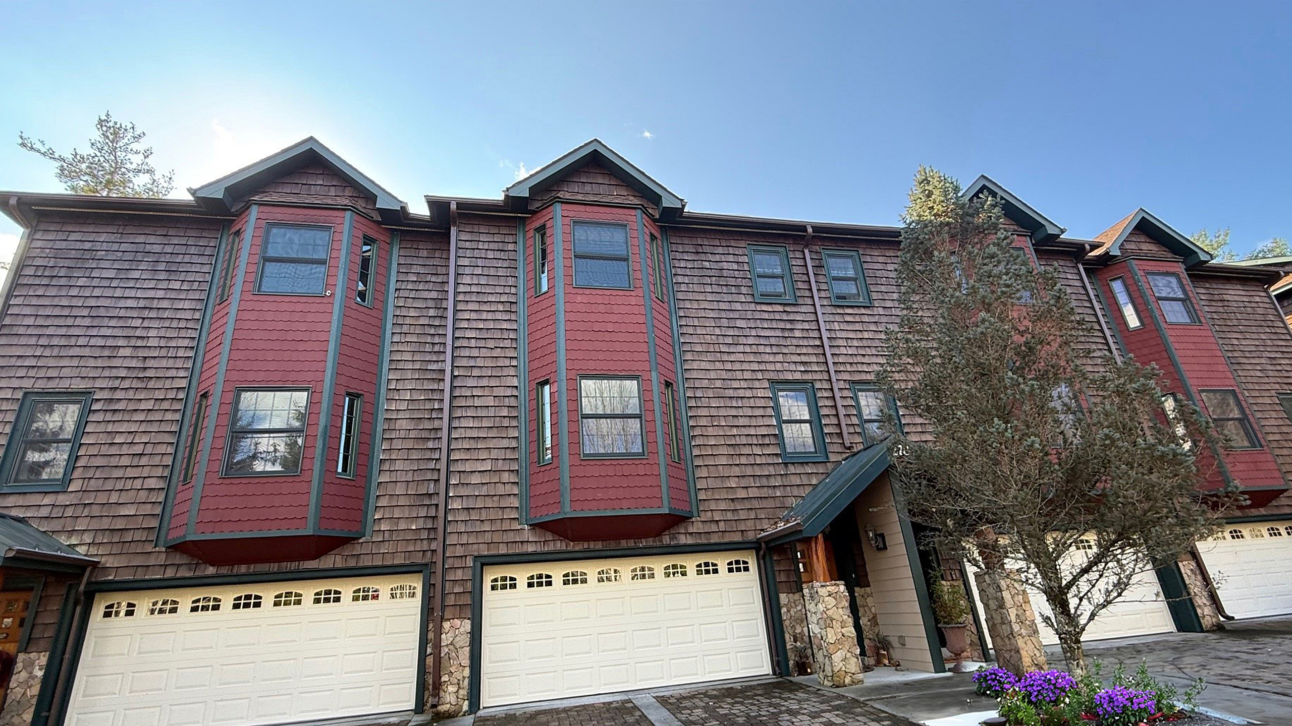 Rustic townhouse with wooden shingles, red bay windows, and two-car garages.