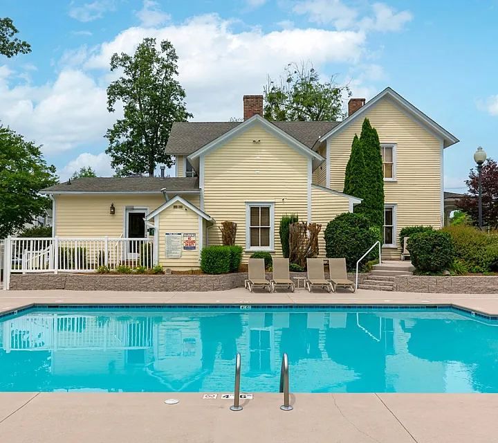 Inviting outdoor swimming pool in front of a quaint yellow house surrounded by lush greenery.