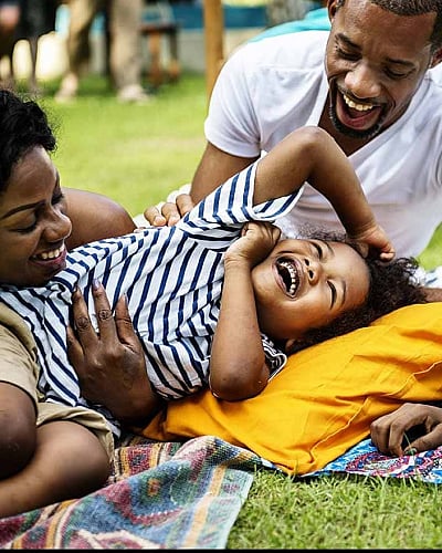 Smiling family enjoying a playful picnic on a grassy lawn with colorful blankets.