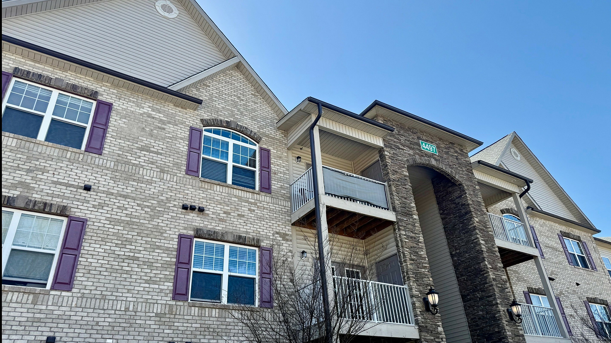 Charming apartment building with modern stone and brick facade, featuring inviting balconies and elegant windows under a clear blue sky.