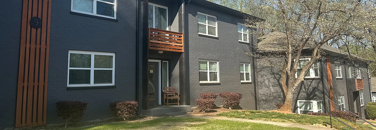 Charming apartment complex with modern design, surrounded by lush greenery and peaceful trees, under a clear blue sky.