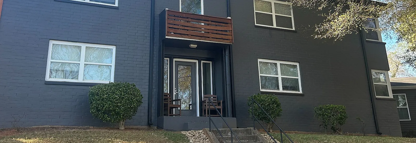 Charming two-story apartment building with modern gray facade, elegant wooden accents, and lush landscaping in a serene neighborhood.