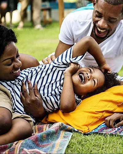 Joyful family enjoying a sunny day outdoors, with a child laughing while surrounded by loving parents and a colorful picnic setup.