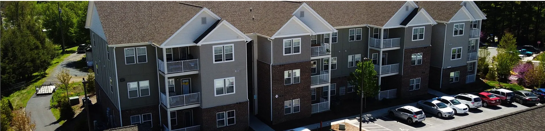 Charming three-story apartment complex with modern exterior and ample parking, nestled in lush greenery.