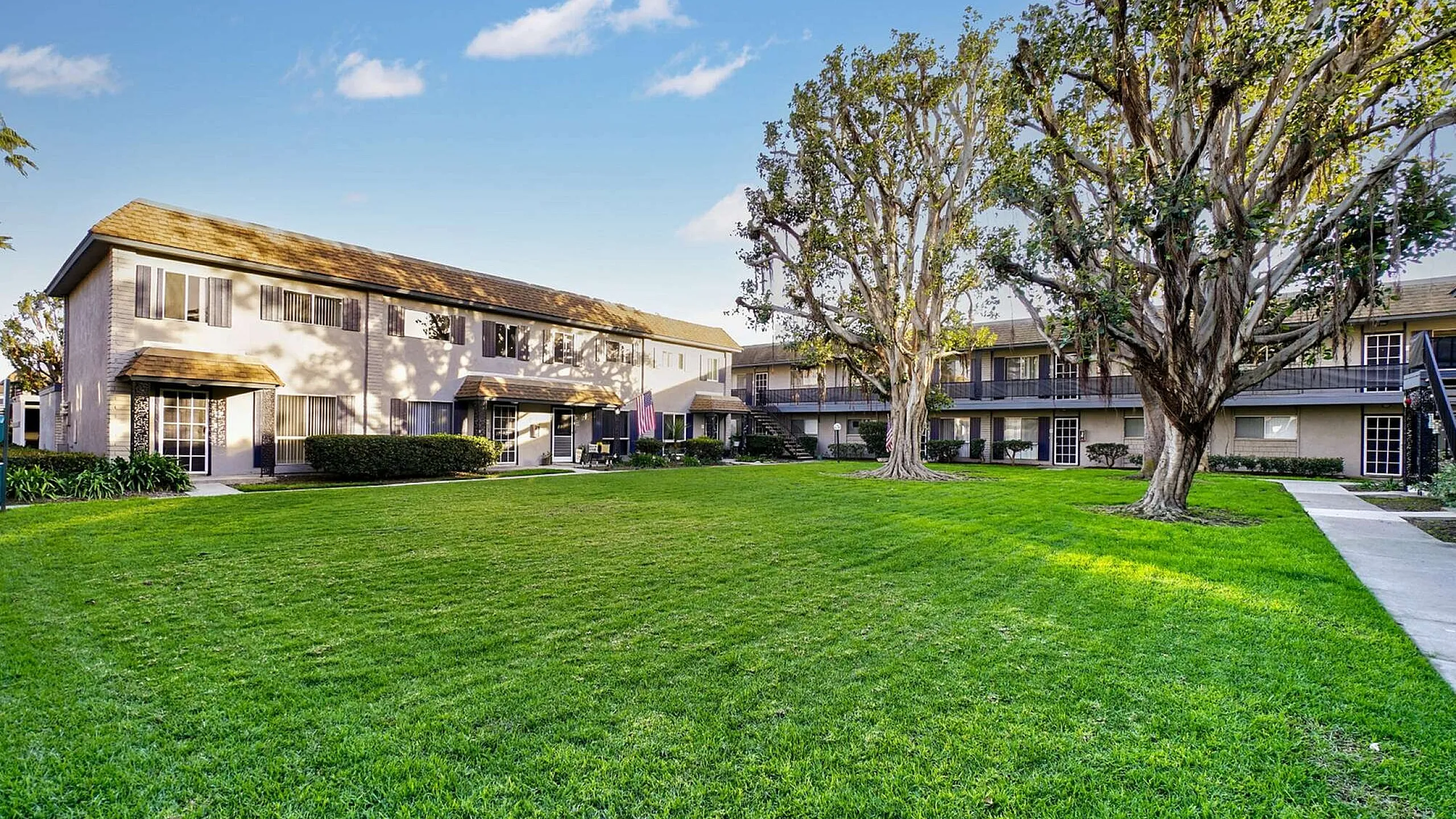 Beautiful apartment complex with spacious green courtyard and mature trees under a clear blue sky.
