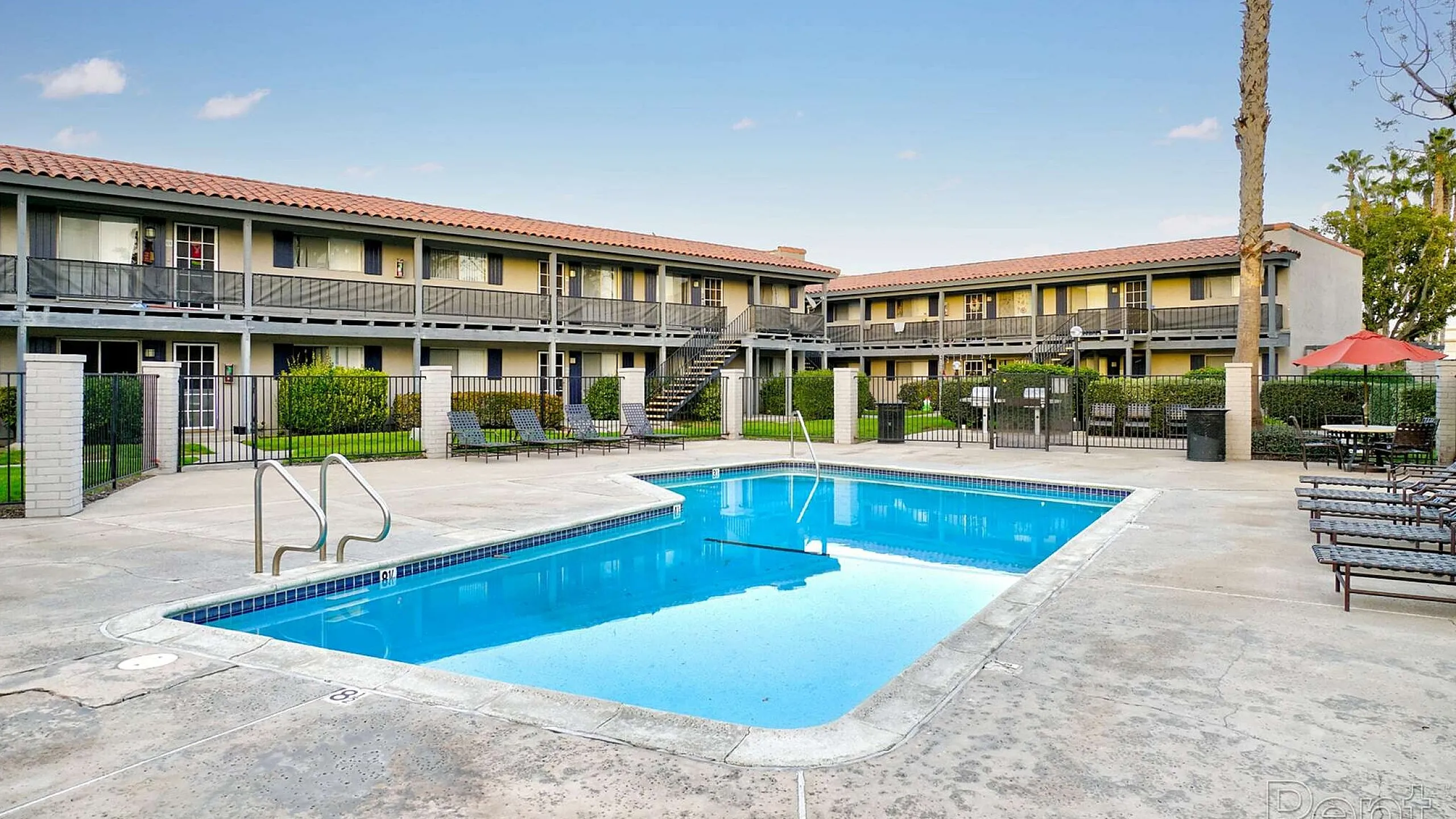 Inviting apartment complex featuring a clear blue swimming pool, surrounded by modern two-story buildings.