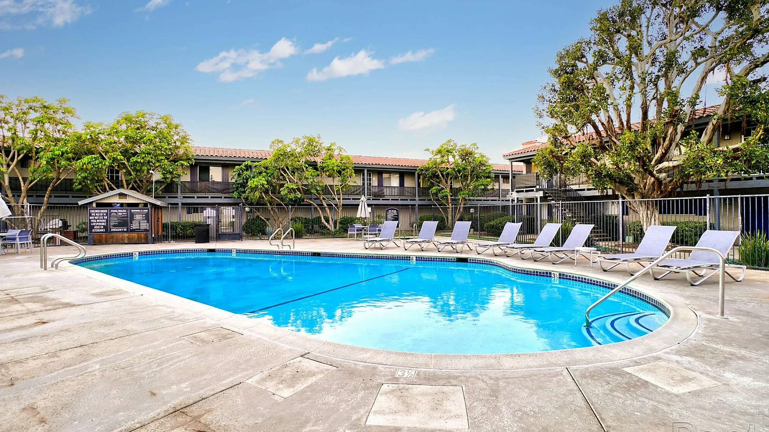 Inviting pool area with sun loungers and lush greenery at a modern apartment complex.
