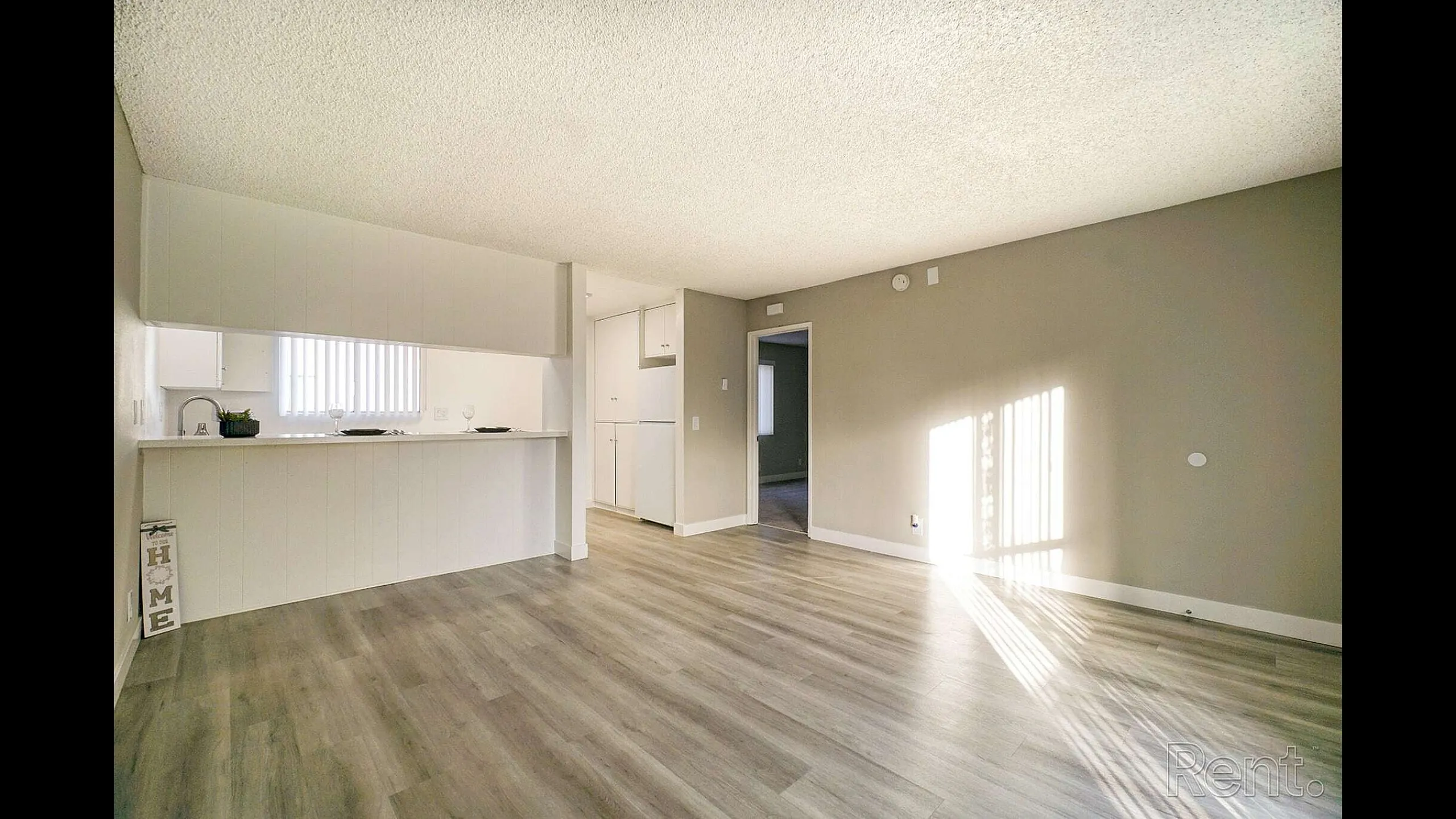 Spacious living area with modern light wood flooring and an open view into a sleek kitchen.