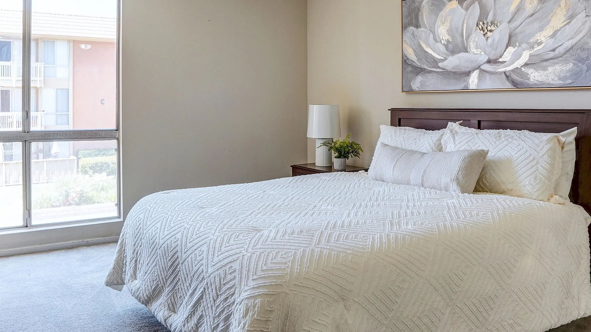 Elegant bedroom with natural light, featuring cozy bed with white textured bedding and modern decor.