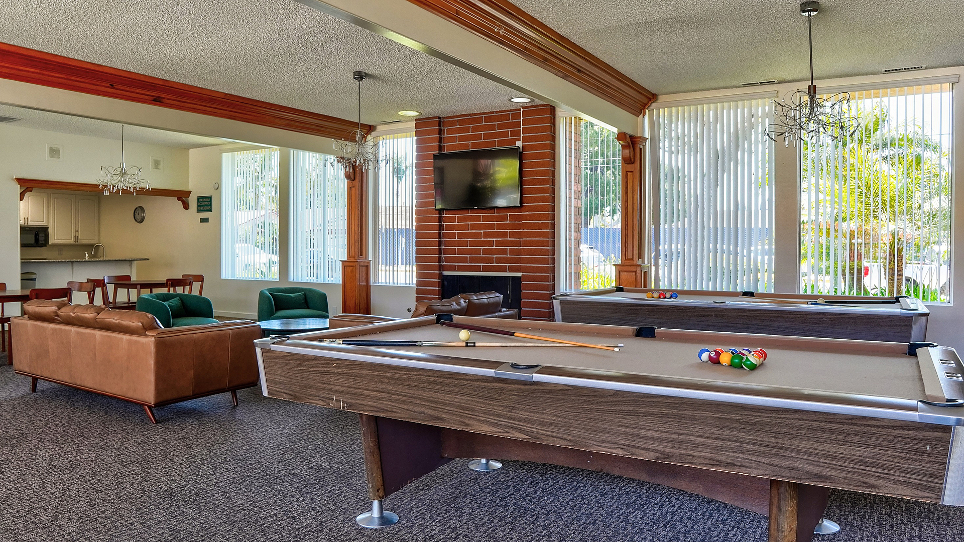 Luxurious apartment amenity room featuring two pool tables, cozy seating area, and a modern kitchen perfect for entertainment.