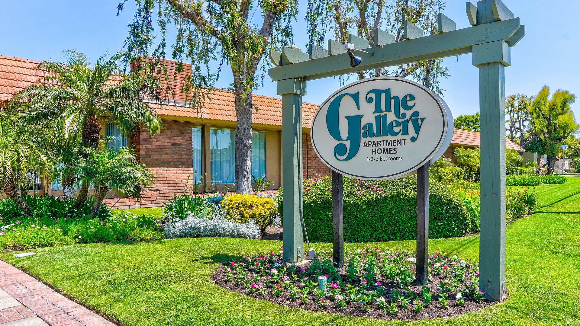 Charming apartment complex with lush landscaping and inviting entrance sign for The Gallery Apartment Homes offering 1-3 bedroom options.
