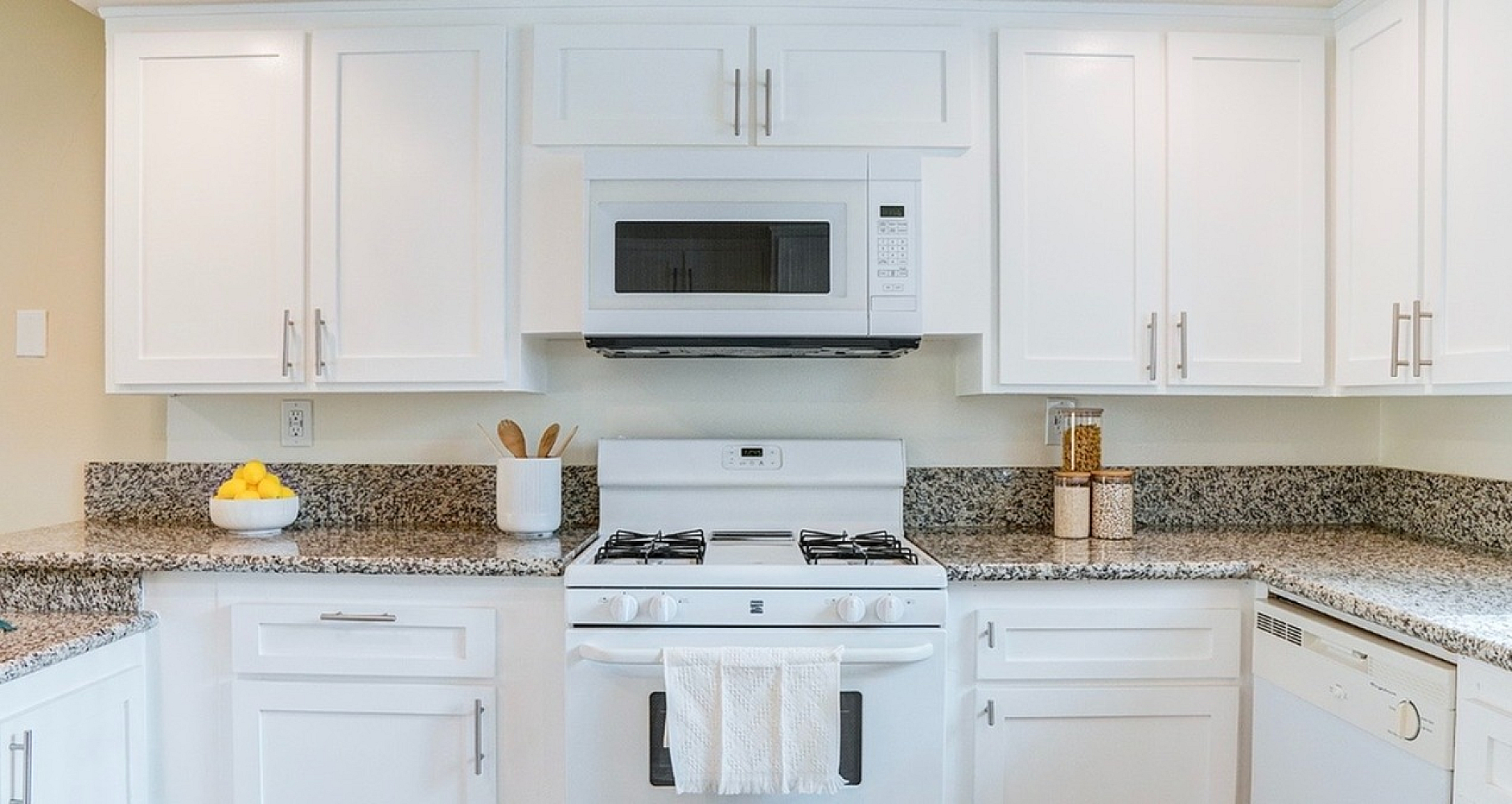 Bright and modern kitchen with sleek white cabinets, granite countertops, and stainless steel appliances including a microwave and gas stove. Ideal for stylish and functional cooking space.