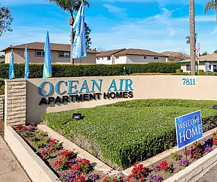 Inviting entrance to Ocean Air Apartment Homes with vibrant landscaping and welcoming signs under sunny skies.