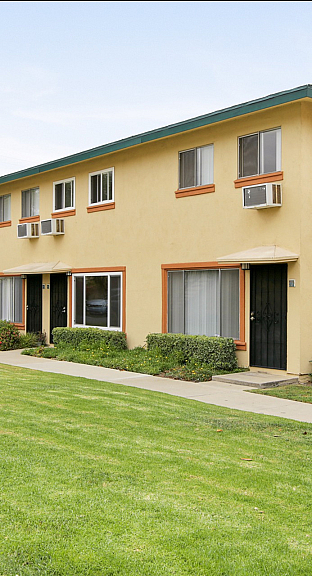 Charming two-story apartment complex with a manicured lawn and vibrant landscaping, featuring spacious windows and individual entrances.