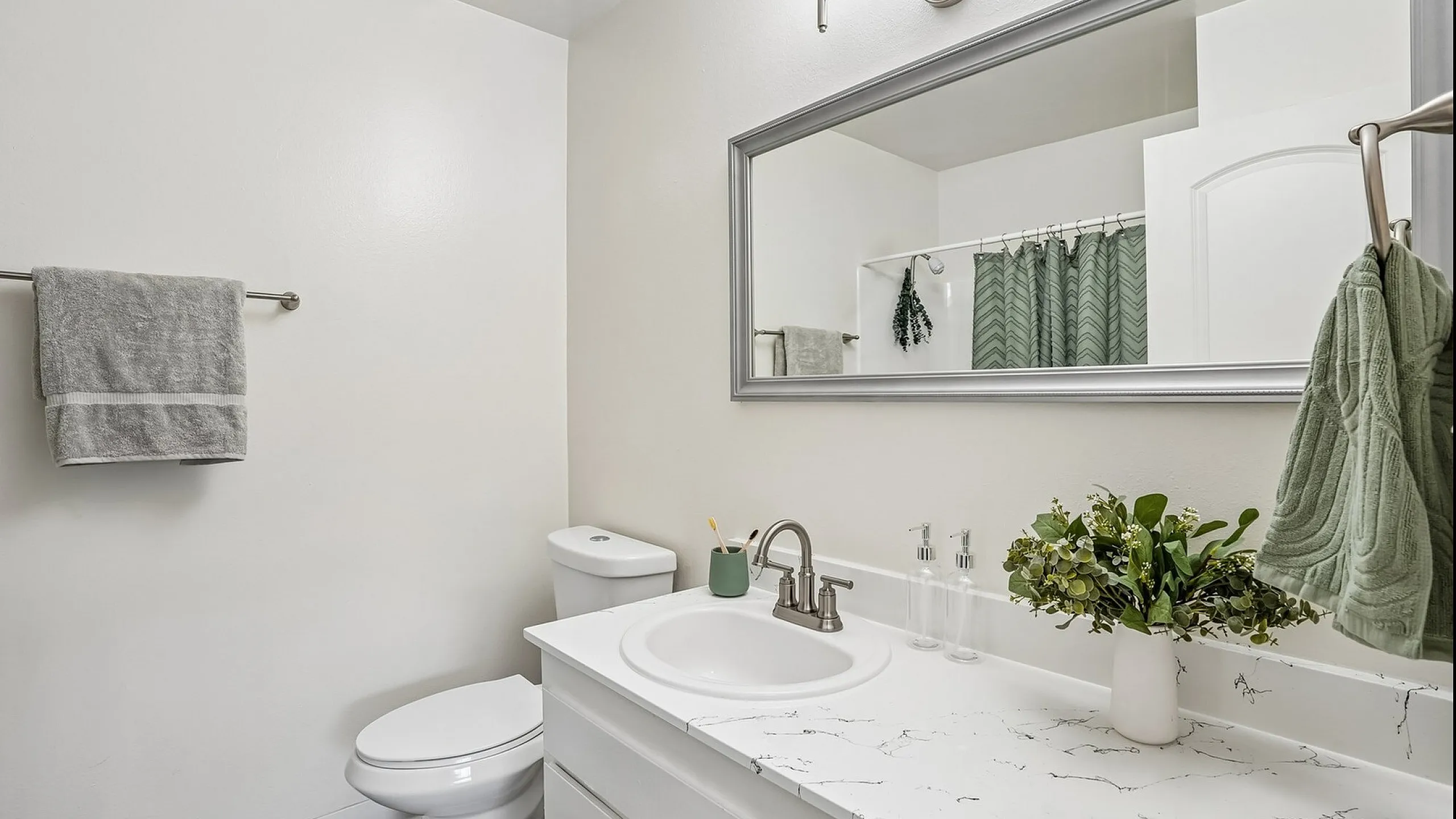Elegant bathroom with a marble-top vanity, large mirror, and chic fixtures, accented by fresh greenery for a tranquil retreat.