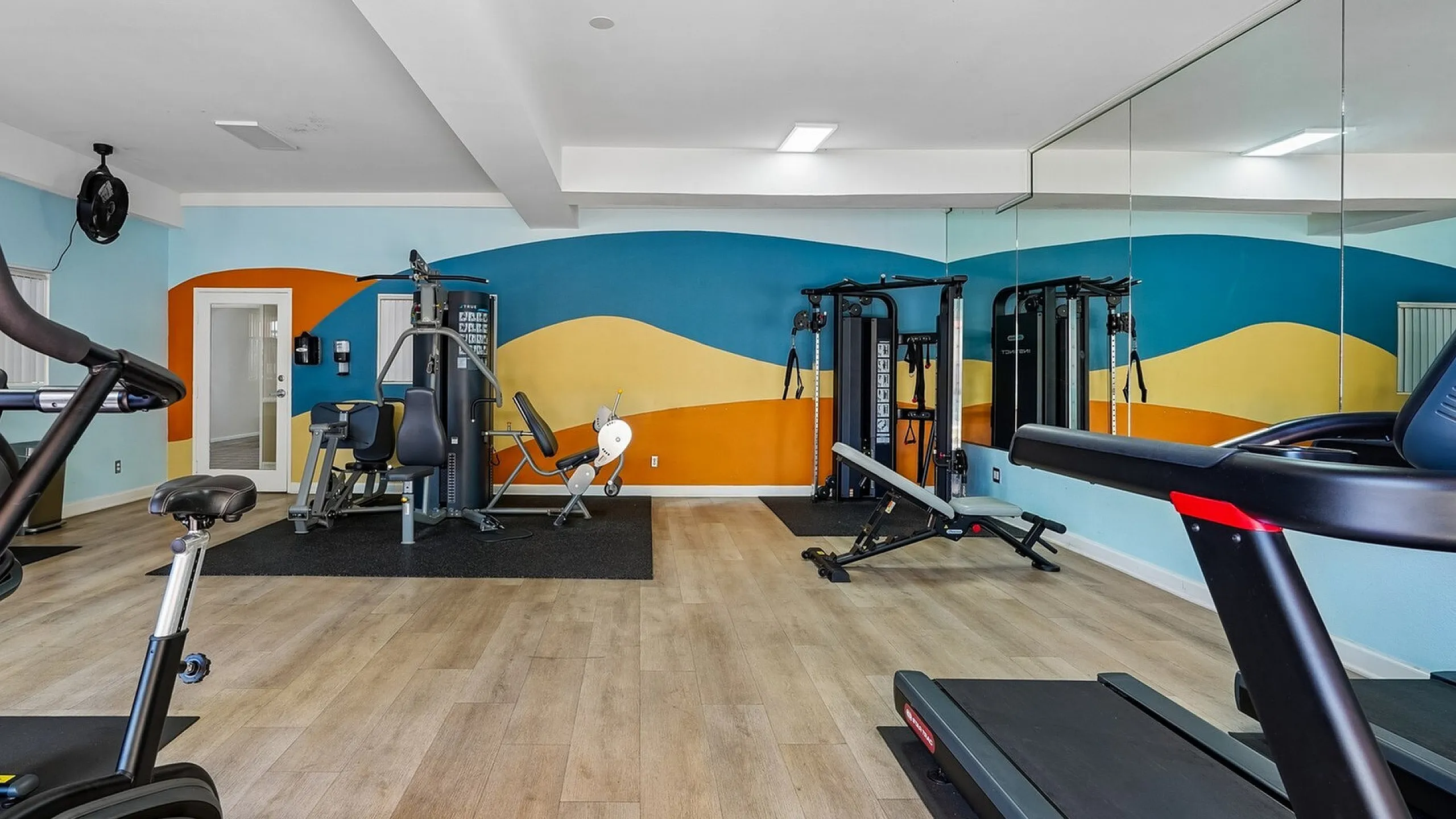 Inviting fitness center with modern exercise equipment, vibrant wall art, and expansive mirrors.