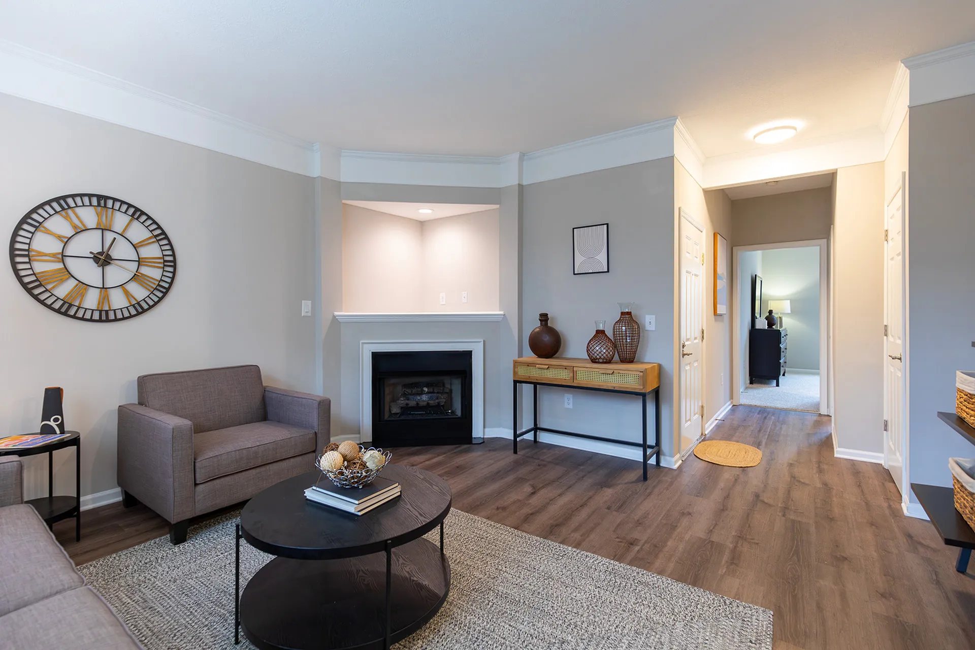 Inviting living room with elegant d&eacute;cor, featuring a cozy fireplace, modern armchair, and stylish wall clock, accentuated by warm wood flooring and tasteful art pieces.
