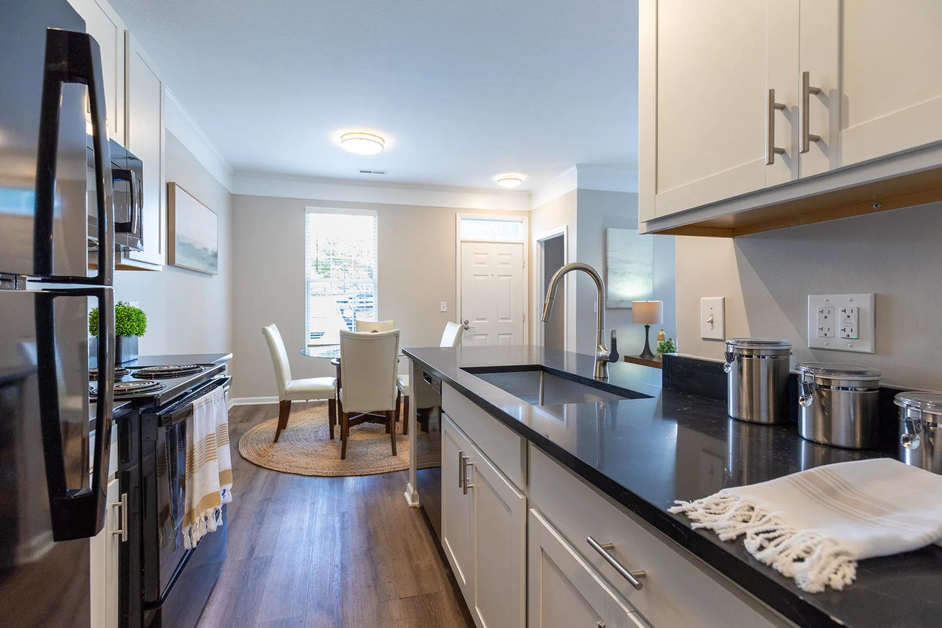 Modern kitchen with sleek black countertops, white cabinetry, and a cozy dining area with natural light.