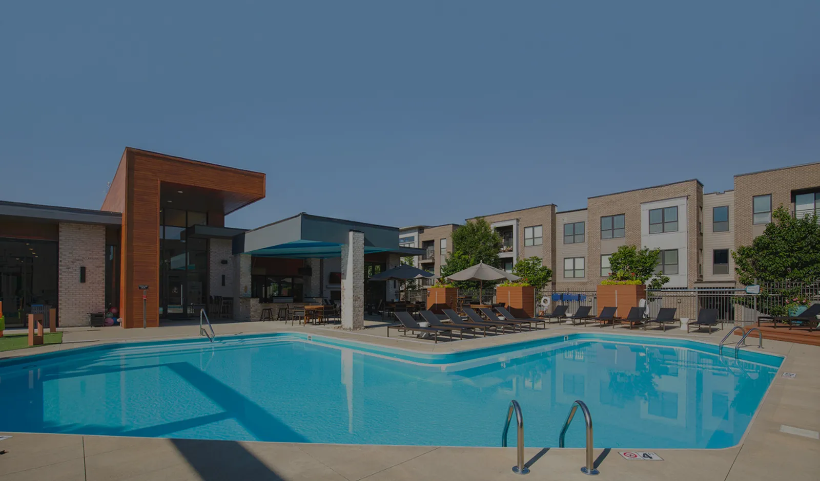 Elegant community pool area with modern sun loungers and umbrellas, spacious apartment complex in the background.