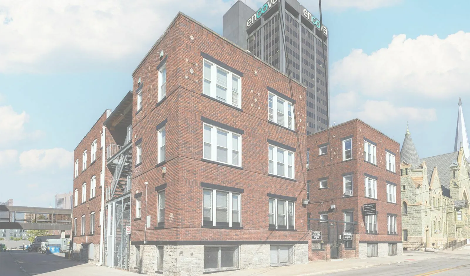 Charming red-brick apartment building with historic architecture and large windows, nestled in an urban setting under a clear blue sky.